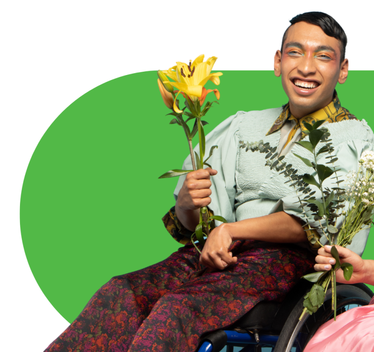 A person is sitting in a wheelchair and smiling at the camera and holding a bunch of yellow flowers.