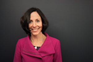 A photo of Megan in a pink blazer smiling at the camera